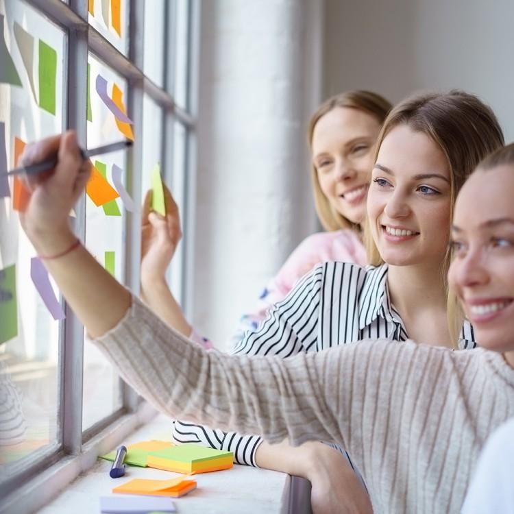 Auszubildene vor Fenster kleben beschriftete Notizzettel an die Scheibe