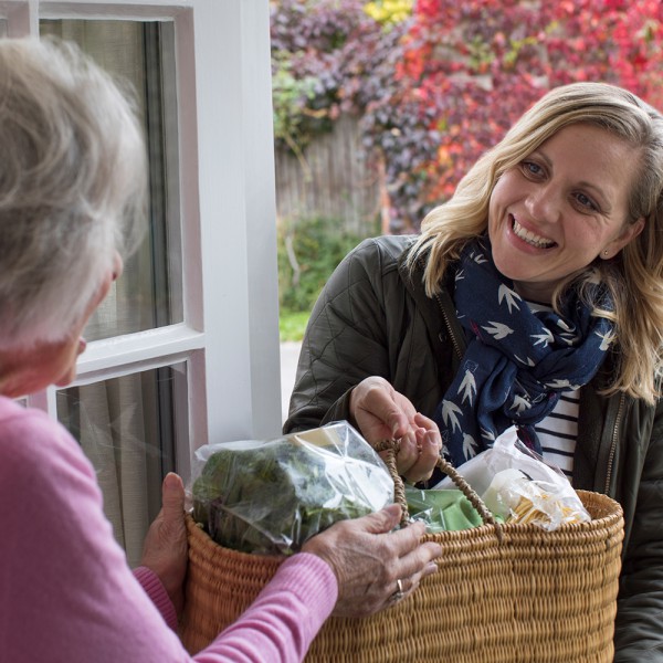 Eine junge Frau überreicht einer älteren Frau den Einkauf