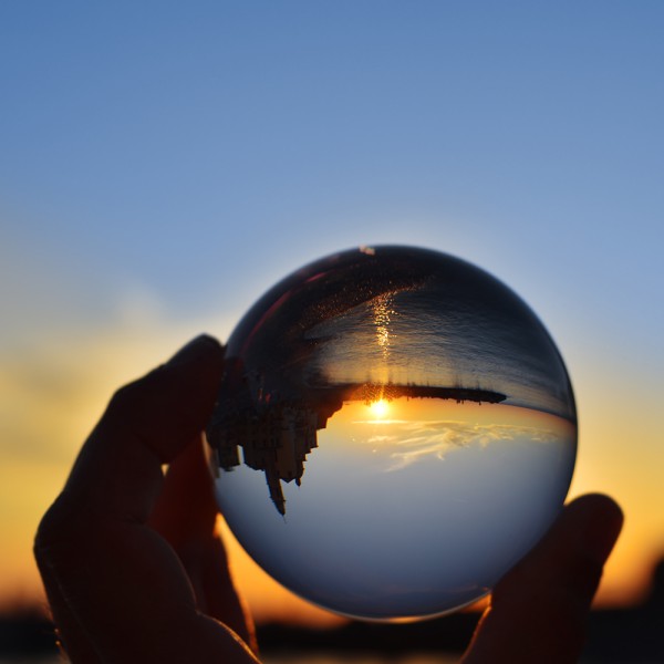 Glaskugel in einer Hand zeigt Landschaft im Sonnenuntergang