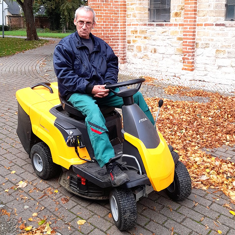 Mitarbeiter auf einem kleinen Fahrzeug beräumt die Wege vom Laub | Copyright: Diakonieverein Burghof e. V.